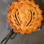 Golden Canadian tourtière meat pie in a cast iron pan with decorative leaf-shaped vents and a flaky browned crust.