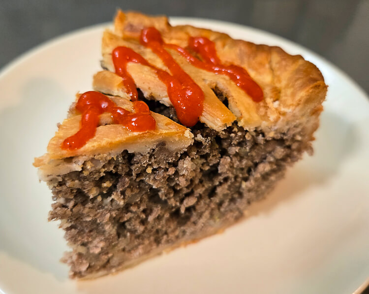 close up photo of a slice of golden Canadian tourtière meat pie topped with a squeeze of ketchup