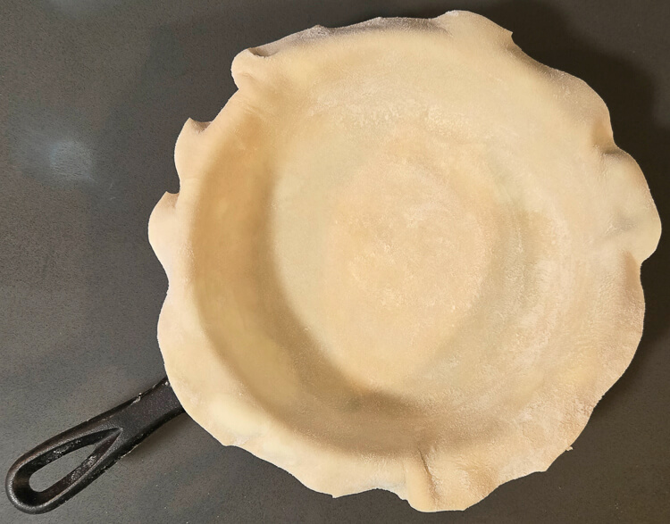 a pie crust fitted inside a cast iron pan