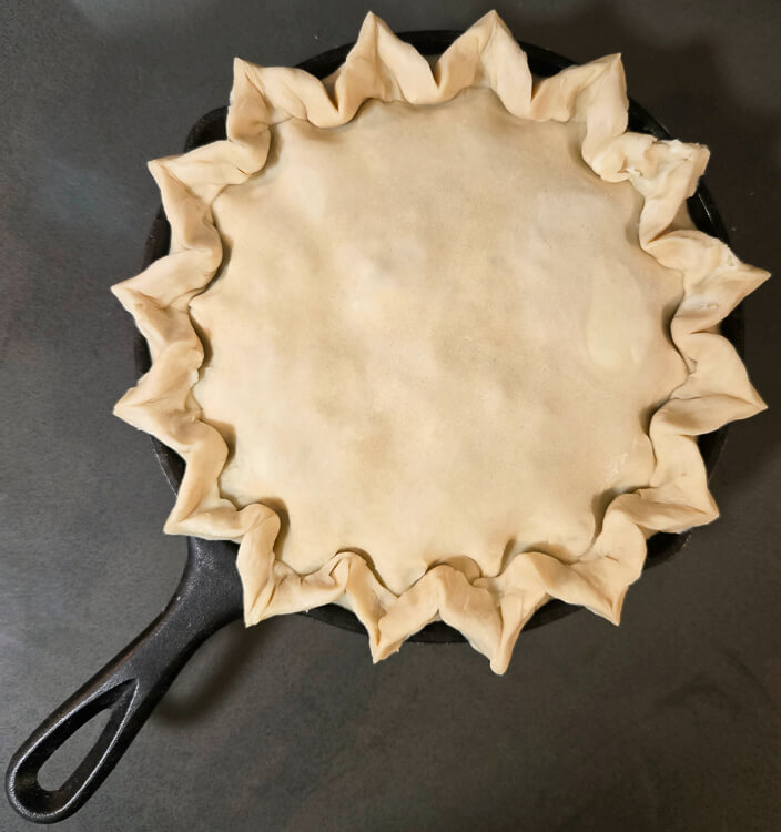 overheat shot of an unbaked pie in a cast iron pan with pointed crimps or flutes