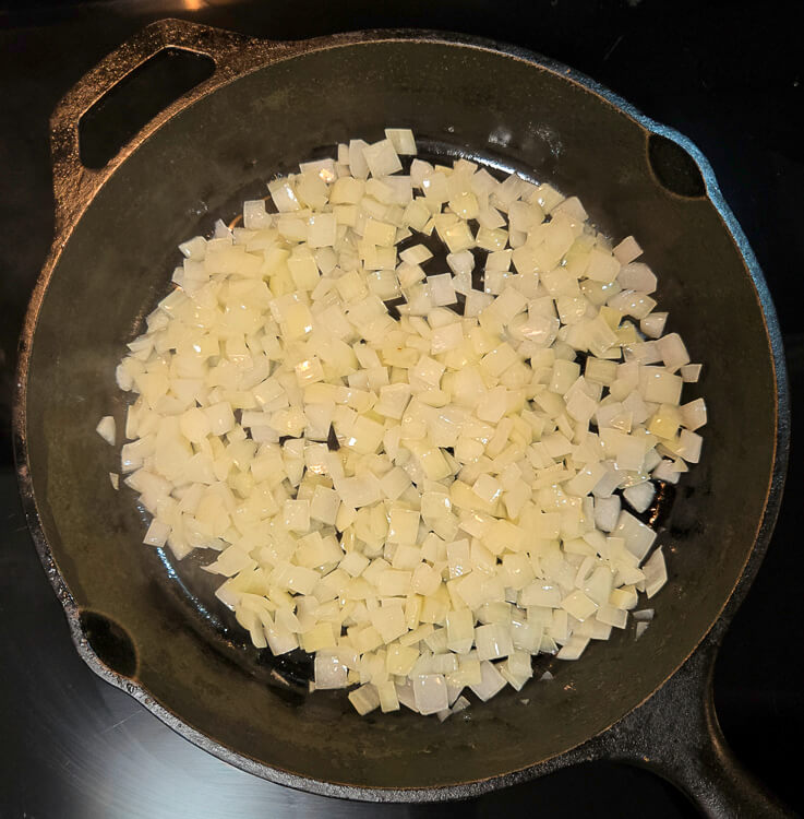 diced onions being sauteed in a cast iron skillet