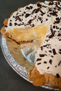 a close up photo of a banana cream pie with a slice cut out so you can see a cross section with flaky crust, creamy homemade vanilla pudding, and whipped cream