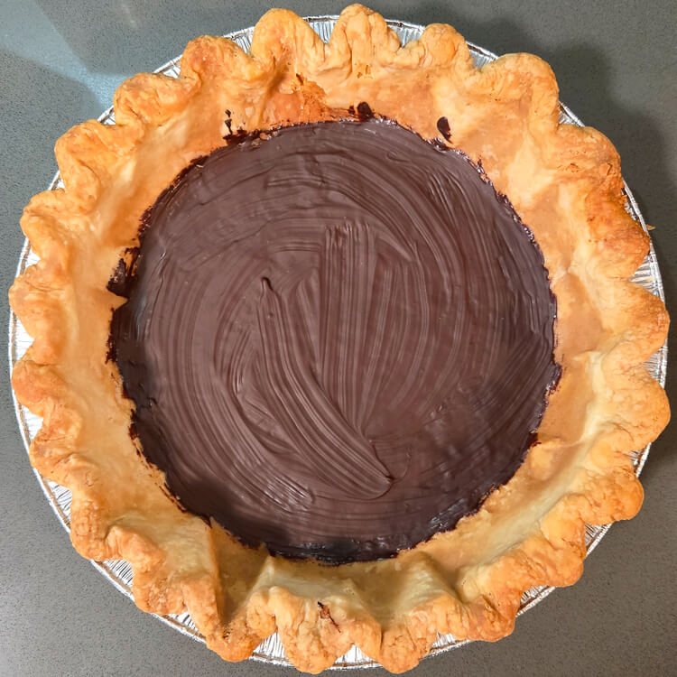 an overhead photo of a blind baked pie shell painted with melted chocolate on the bottom for banana cream pie or other cream pies