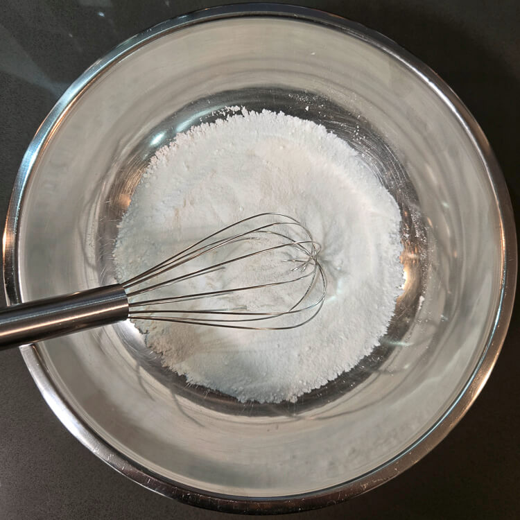 an overhead photo of mixed dry ingredients in a metal mixing bowl with a balloon whisk