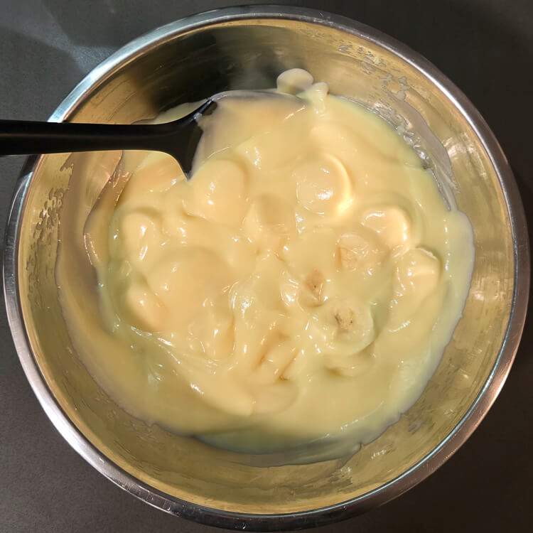 homemade vanilla pudding mixed with banana slices in a metal mixing bowl for banana cream pie or banana pudding