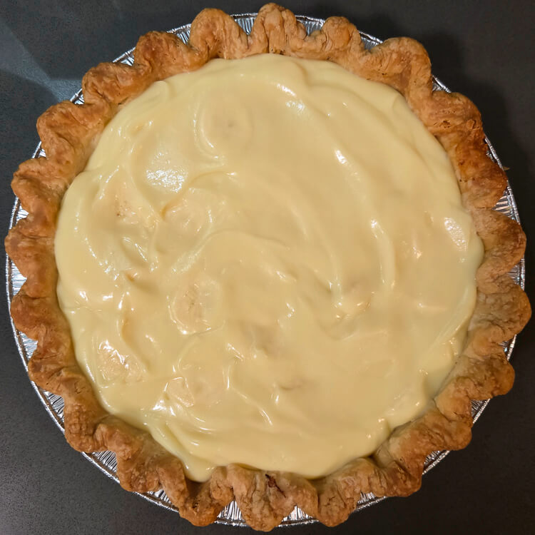an overhead photo of a banana cream pie with no topping. Homemade vanilla pudding with banana slices mixed in poured into a blind baked pie crust with crimped edges