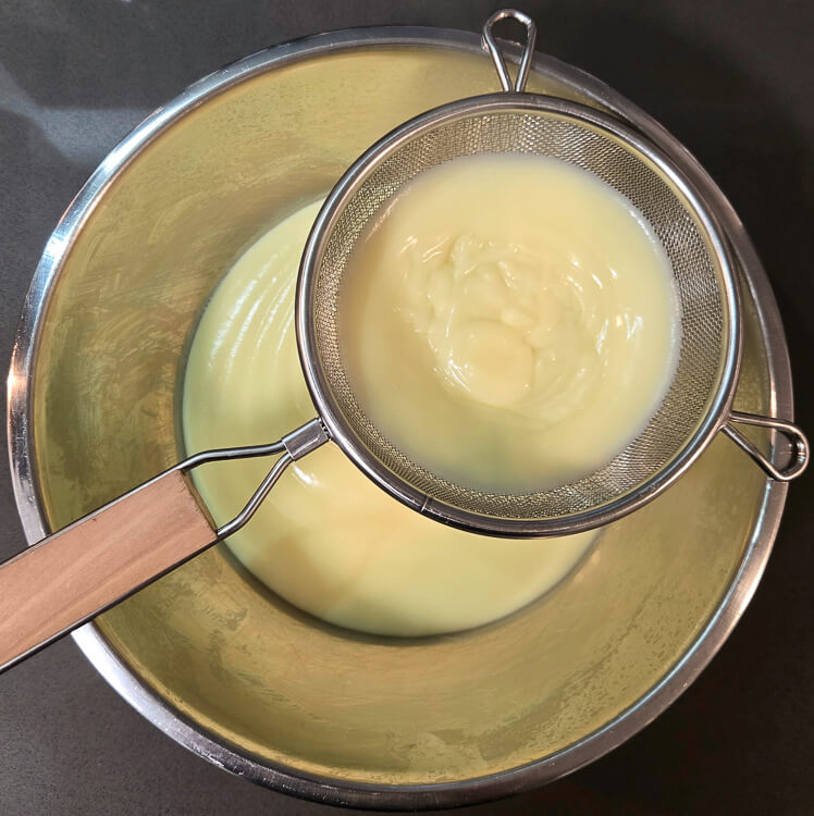 an overhead photo of straining freshly made homemade vanilla pudding through a fine-mesh sieve