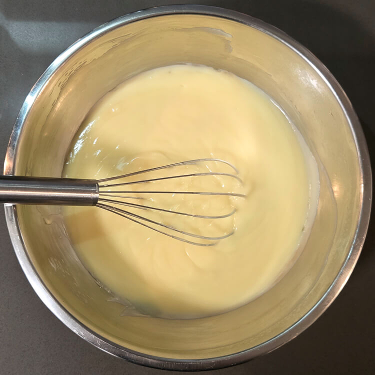 an overhead photo of creamy homemade vanilla pudding in a metal mixing bowl with a balloon whisk