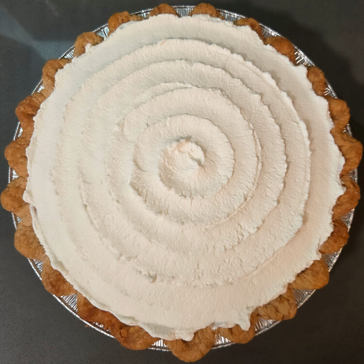 an overhead photo of a banana cream pie topped with whipped cream in a spiral pattern in a crimped pie crust