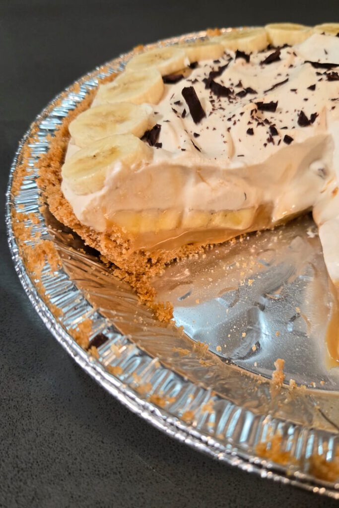 a close up photo of a banoffee pie with a slice cut out so you can see the banana slices and dulce de leche beneath the top layer of coffee flavored whipped cream