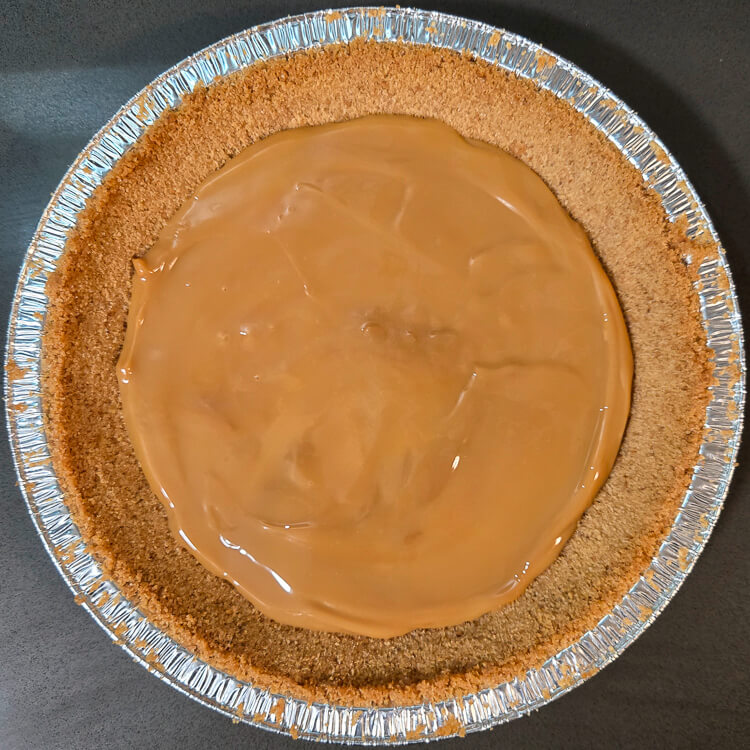 overhead photo of dulce de leche spread inside of the bottom of a digestive biscuit pie crust. This is the first step in assembling a banoffee pie.