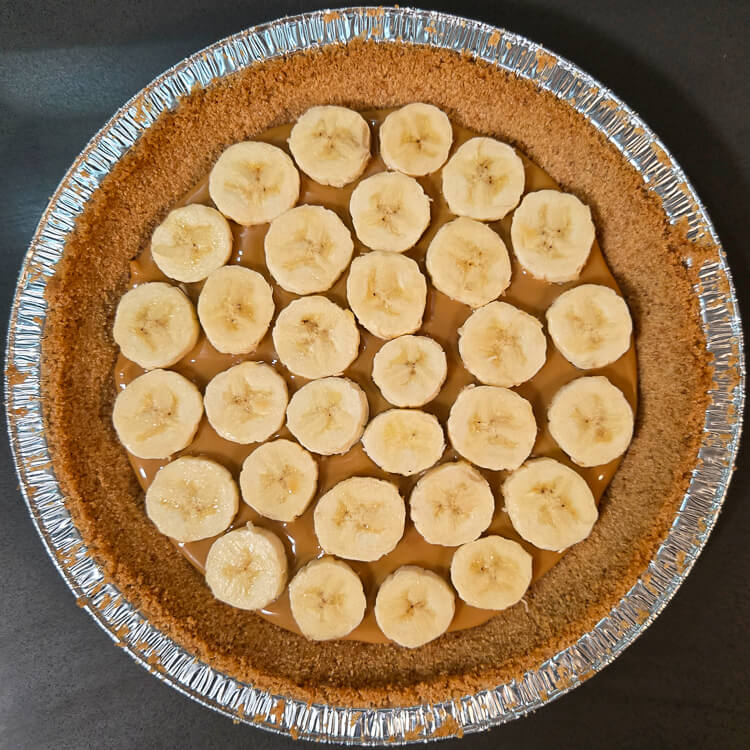 an overhead photo of a digestive biscuit crust with a layer of dulce de leche caramel spread over the bottom and banana slices laid out over the caramel