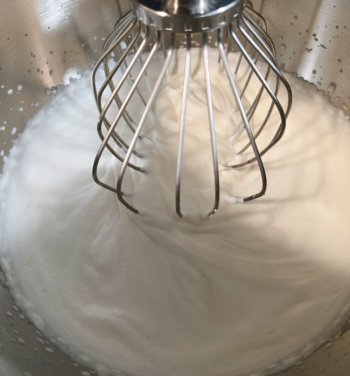 a close up photo of freshly whipped cream in a stand mixer with a whisk attachment