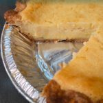 Slice of homemade buttermilk pie in a metal pie tin with a creamy custard filling and golden brown crust.