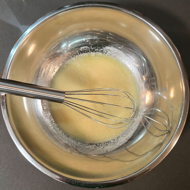 a metal mixing bowl with a metal whisk mixing together melted butter and flour
