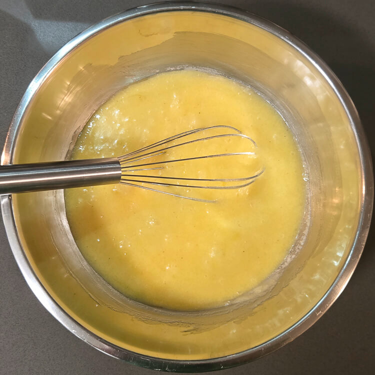 a metal mixing bowl with metal whisk with egg, sugar, and butter whisked together
