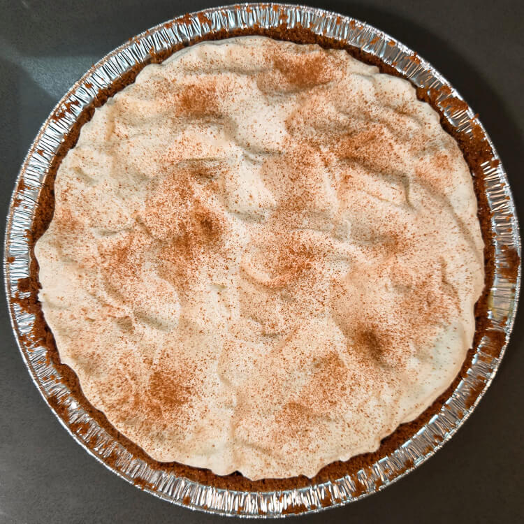 overhead photo of an eggnog cream pie in a gingersnap crust with whipped cream topping dusted with cinnamon