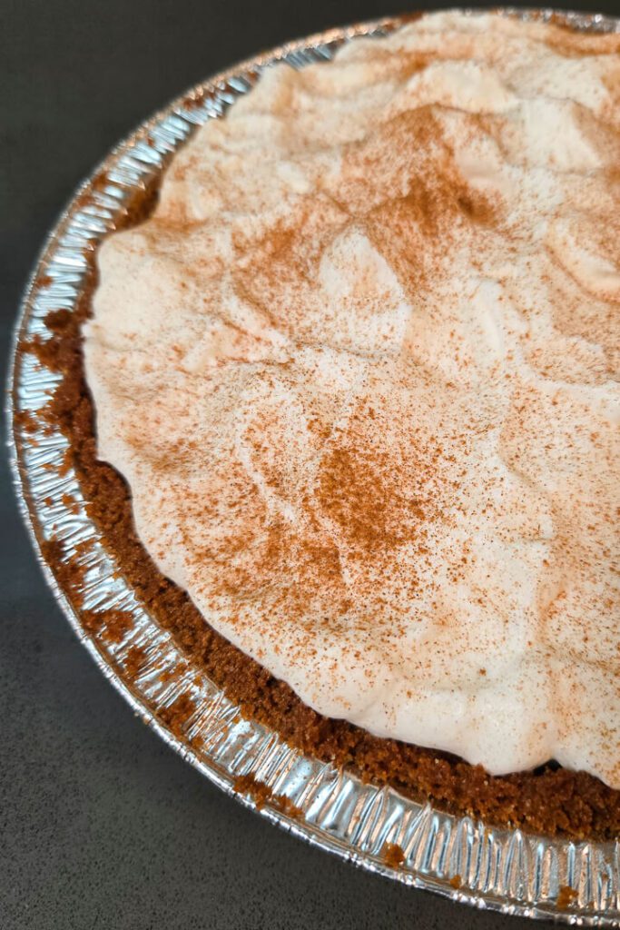 close up photo of an eggnog cream pie in a gingersnap crust with whipped cream topping dusted with cinnamon