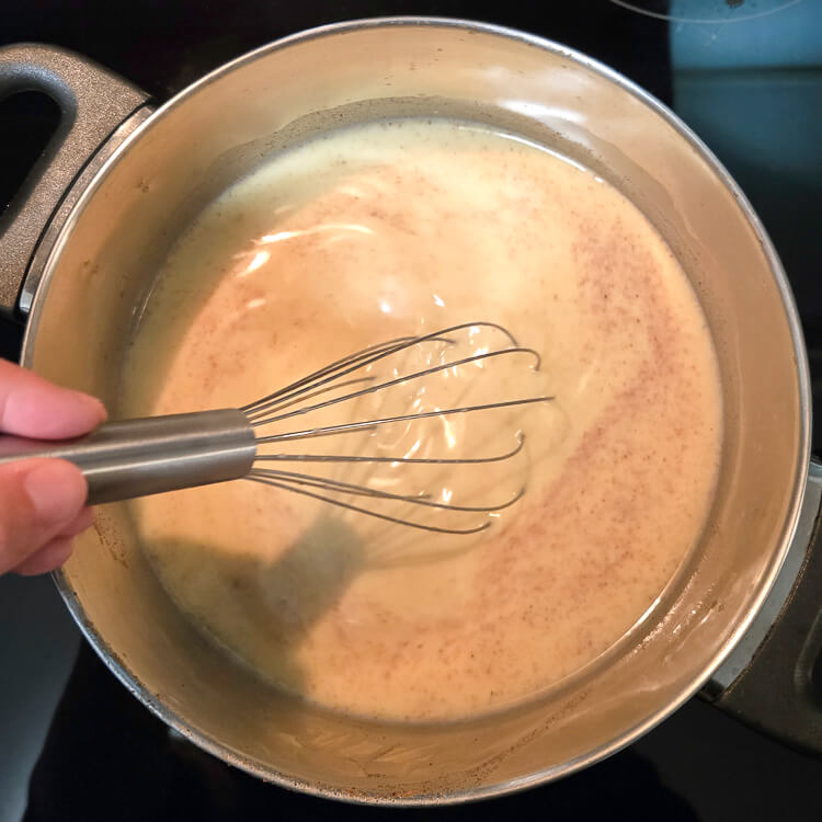 an overhead photo of homemade eggnog pudding being made on a stovetop with a whisk