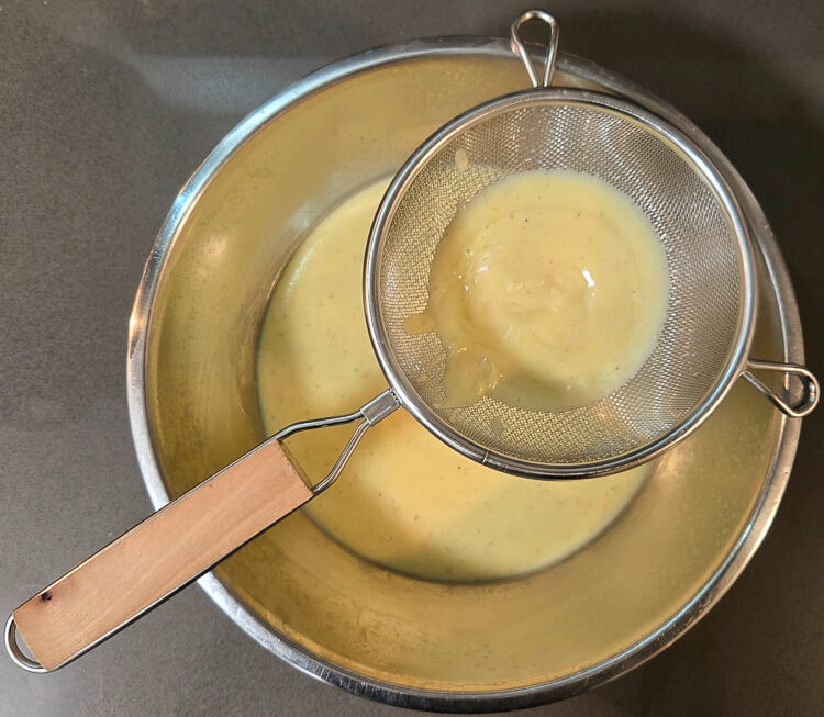 freshly made homemade eggnog pudding being strained through a fine-mesh sieve