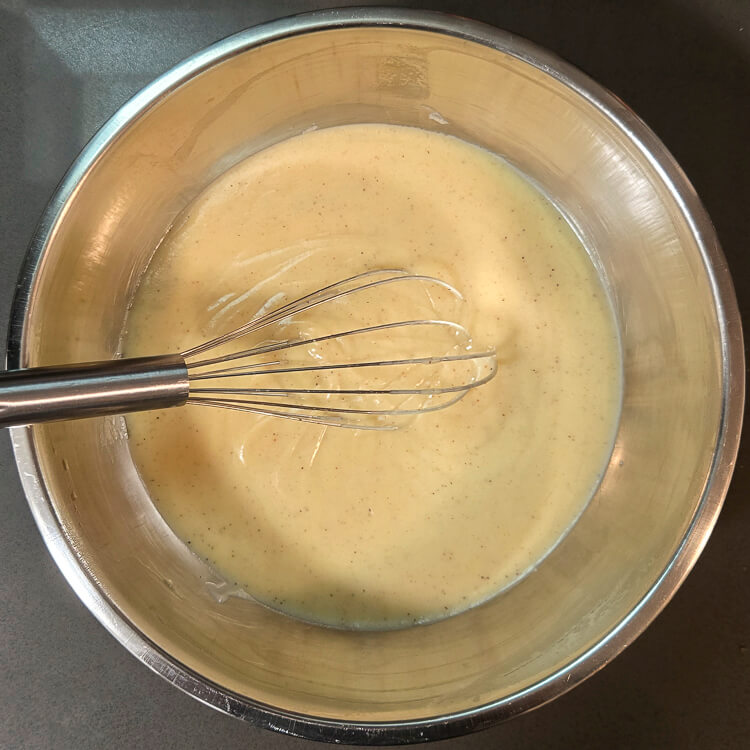 freshly made homemade eggnog pudding in a mixing bowl with a metal whisk