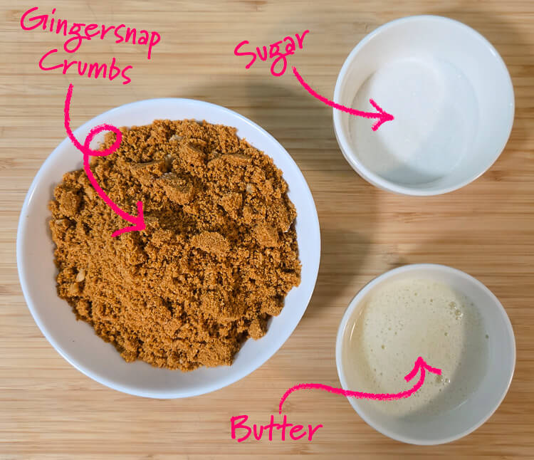 ingredients for a gingerbread cookie crust on a cutting board with text labels: gingersnap crumbs, sugar, and melted butter