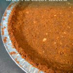 Close-up of a homemade gingersnap pie crust in a metal pie tin, showing its crisp, spiced crumb texture.