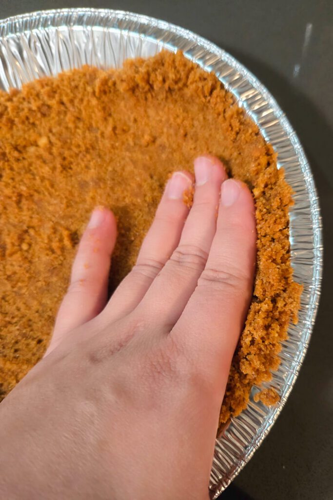 close up photo showing how to press cookie or crackers crumbs into a pie tin to make a pie crust