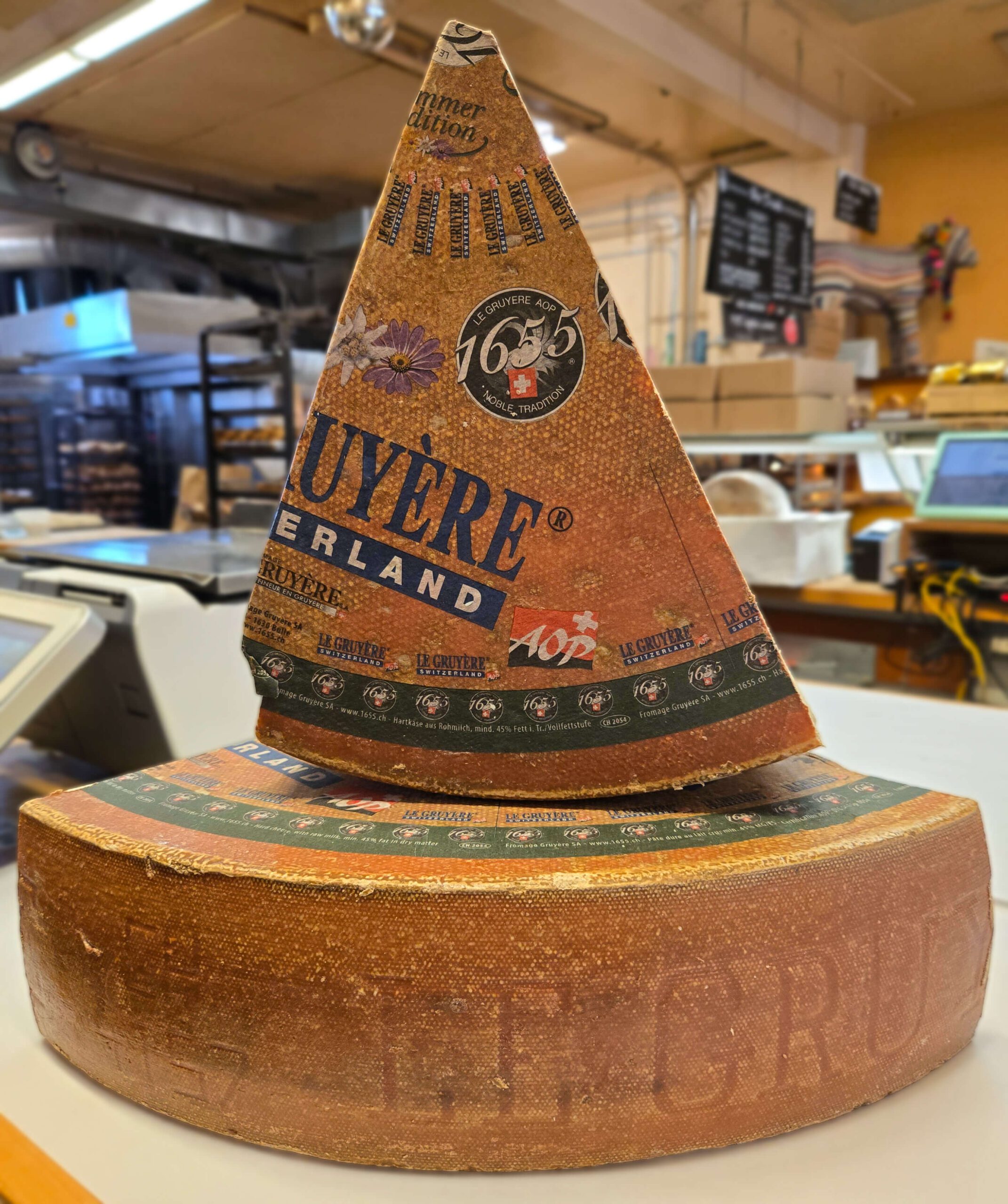 a quarter wheel of Gruyere AOP with a wedge sitting on top in a cheese shop