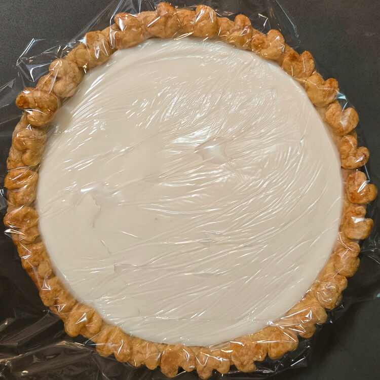 an overheat photo of a pie with hot cream filling and a piece of plastic wrap pressed to the top so it cools without developing a skin