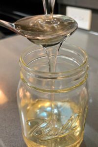 clear invert sugar syrup being poured over a spoon into a glass mason jar