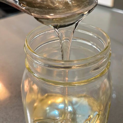 clear invert sugar syrup being poured over a spoon into a glass mason jar