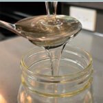 A spoonful of clear invert sugar syrup being poured into a glass jar, with simple glucose, fructose, and sucrose molecule diagrams shown below the image.