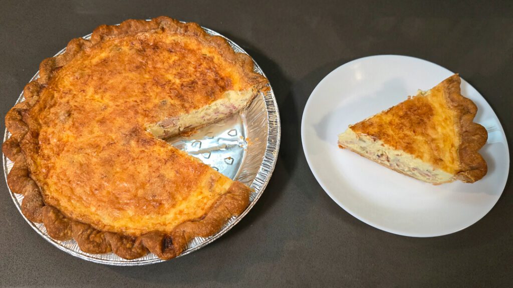 an overhead photo of a quiche lorraine with a slice cut out and placed on a white plate next to it