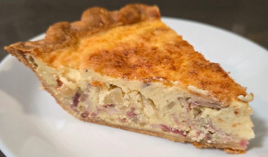 a close up photo of a slice of quiche lorraine with onions, bacon, and gruyere