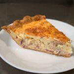 a close up photo of a slice of quiche lorraine with onions, bacon, and gruyere