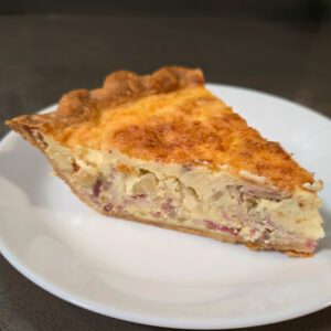 a close up photo of a slice of quiche lorraine with onions, bacon, and gruyere