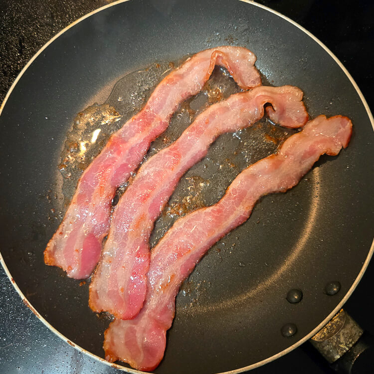 three strips of bacon being fried in a frying pan