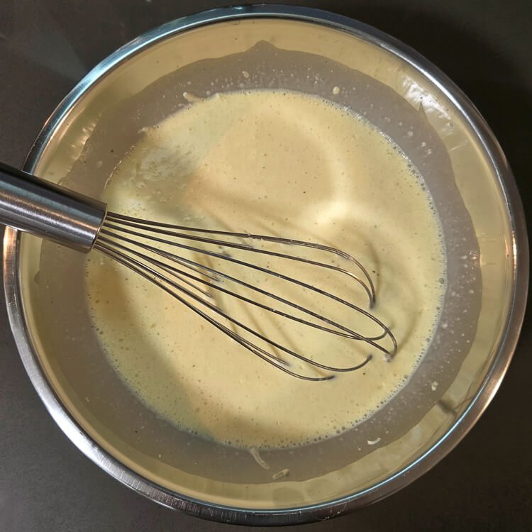 an overhead photo of a metal mixing bowl with a metal whisk whisking together quiche batter