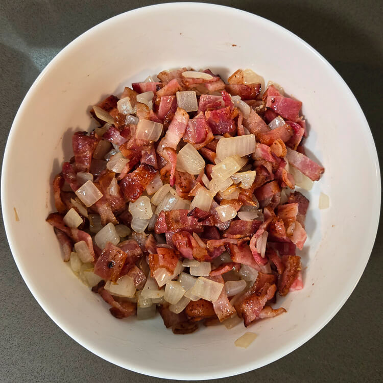 an overhead photo of bacon bits and sauteed diced onion in a white bowl