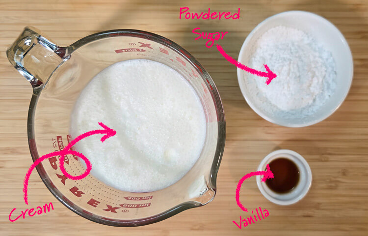 ingredients for whipped cream laid out on a wooden cutting board with text labels: cream, vanilla, powdered sugar