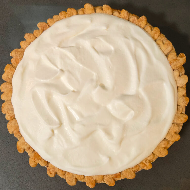 an overhead photo of an unsliced chocolate haupia pie topped with whipped cream in a crust with hearts around the edge