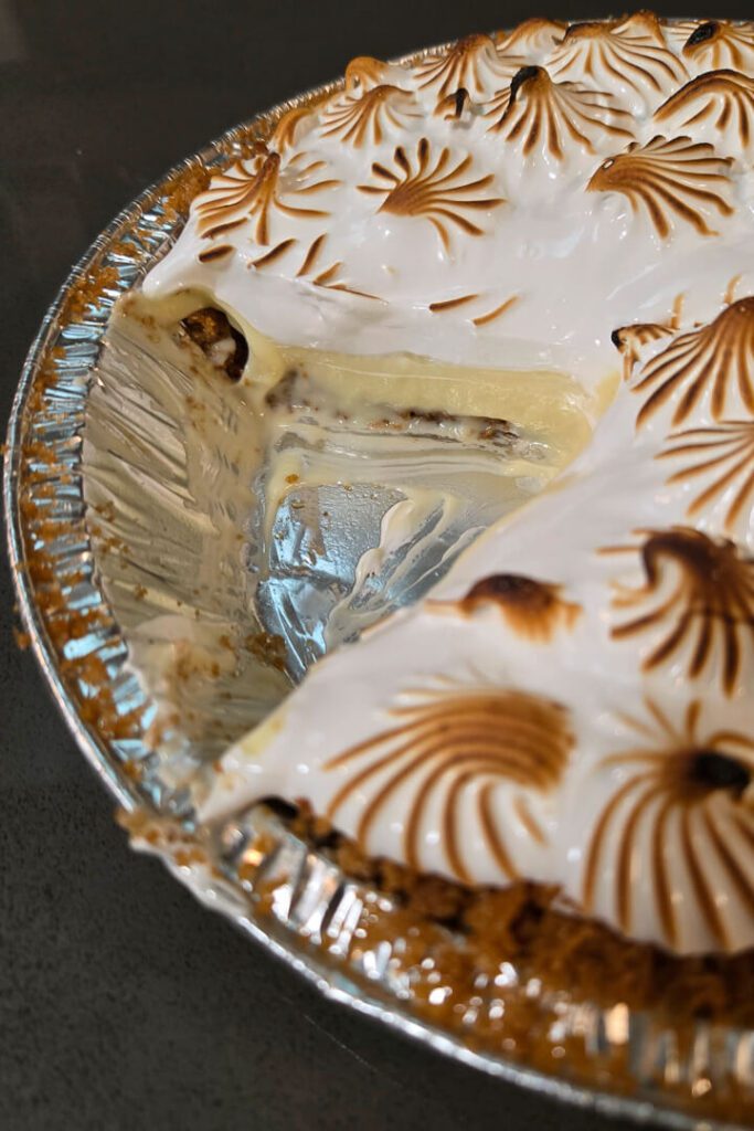 close up photo of a cross section of flapper pie with a slice cut out showing graham cracker crust, homemade old-fashioned vanilla pudding, and a meringue topping