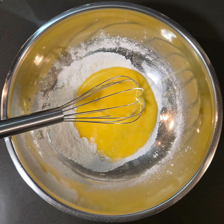 an overhead photo showing egg yolks partially mixed with dry ingredients for vanilla pudding