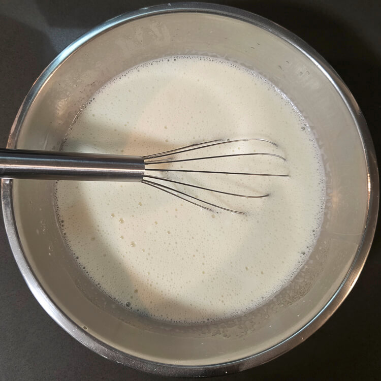 overhead photo of uncooked vanilla pudding after tempering the eggs and mixing all of the ingredients together in a metal mixing bowl with a metal whisk
