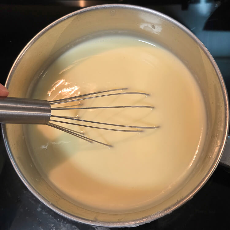 overhead view of vanilla pudding being cooked on the stovetop in a pot with a metal whisk