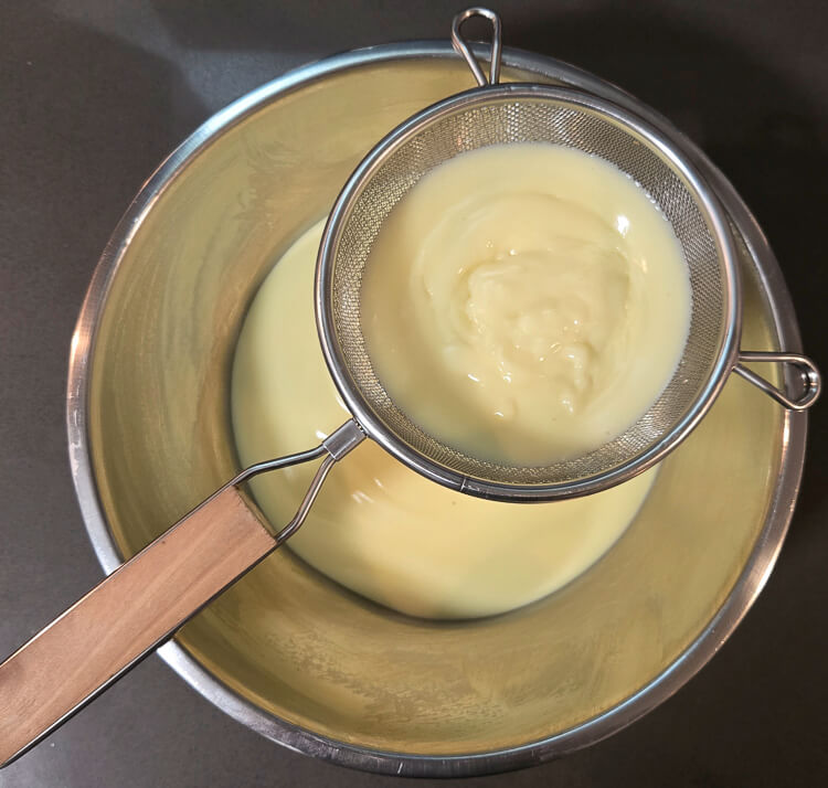 freshly made homemade vanilla pudding being strained through a fine mesh strainer