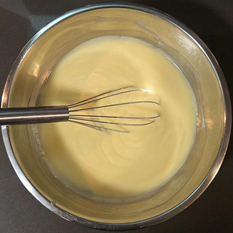 freshly made homemade vanilla pudding in a metal mixing bowl with a metal whisk