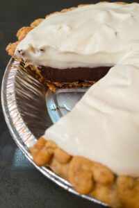 close up photo of a chocolate haupia pie with a slice cut out showing a cross section with layers of golden pie crust, chocolate haupia, coconut haupia, and whipped cream