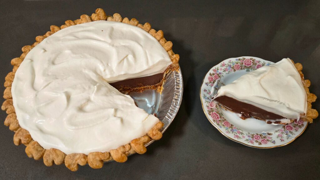 overhead photo of a chocolate haupia pie with a slice cut out and placed next to it on a floral antique plate